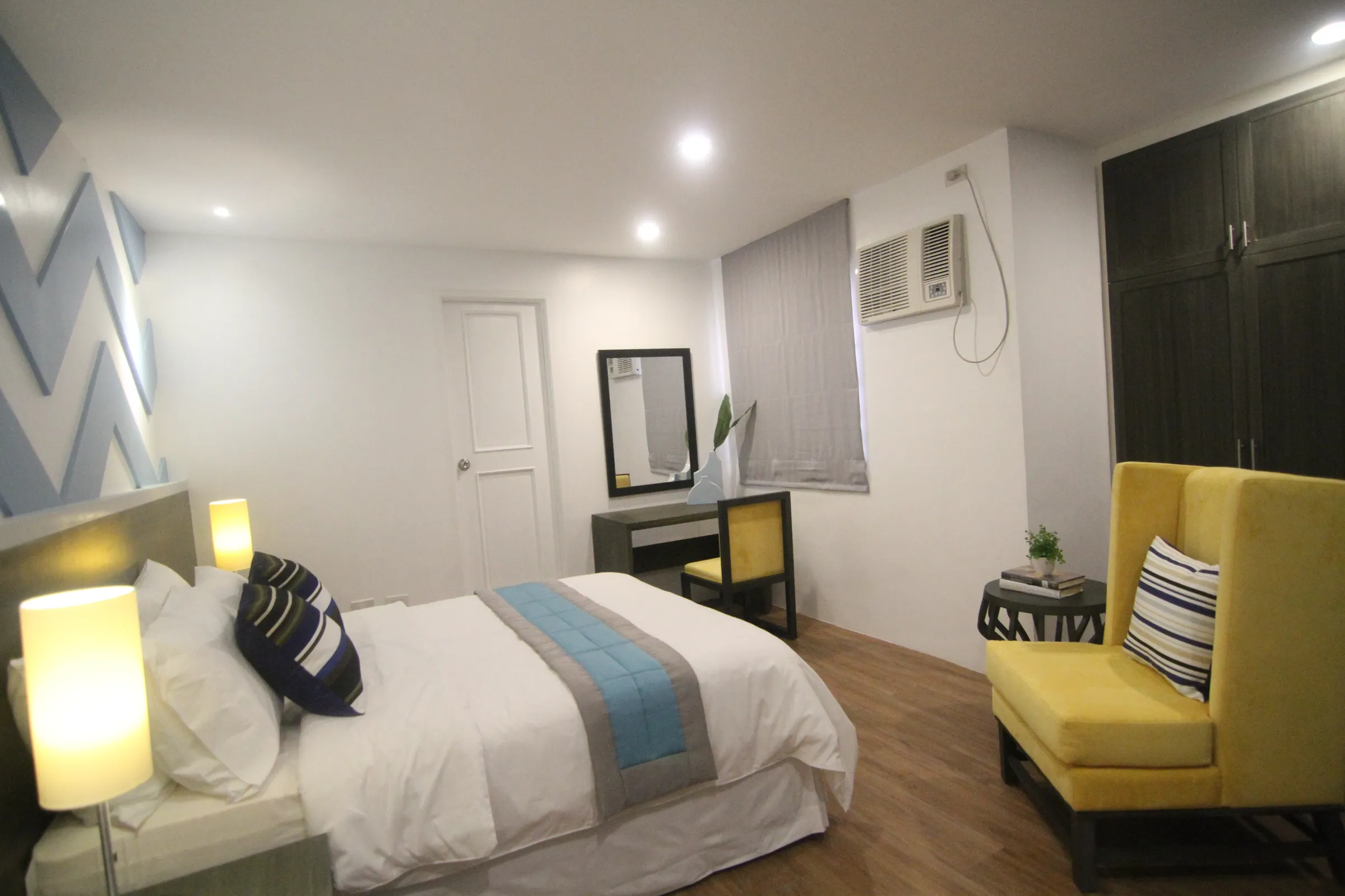 The Deluxe Queen room — a queen bed with accent chairs, warm wood floors and soft daylight.